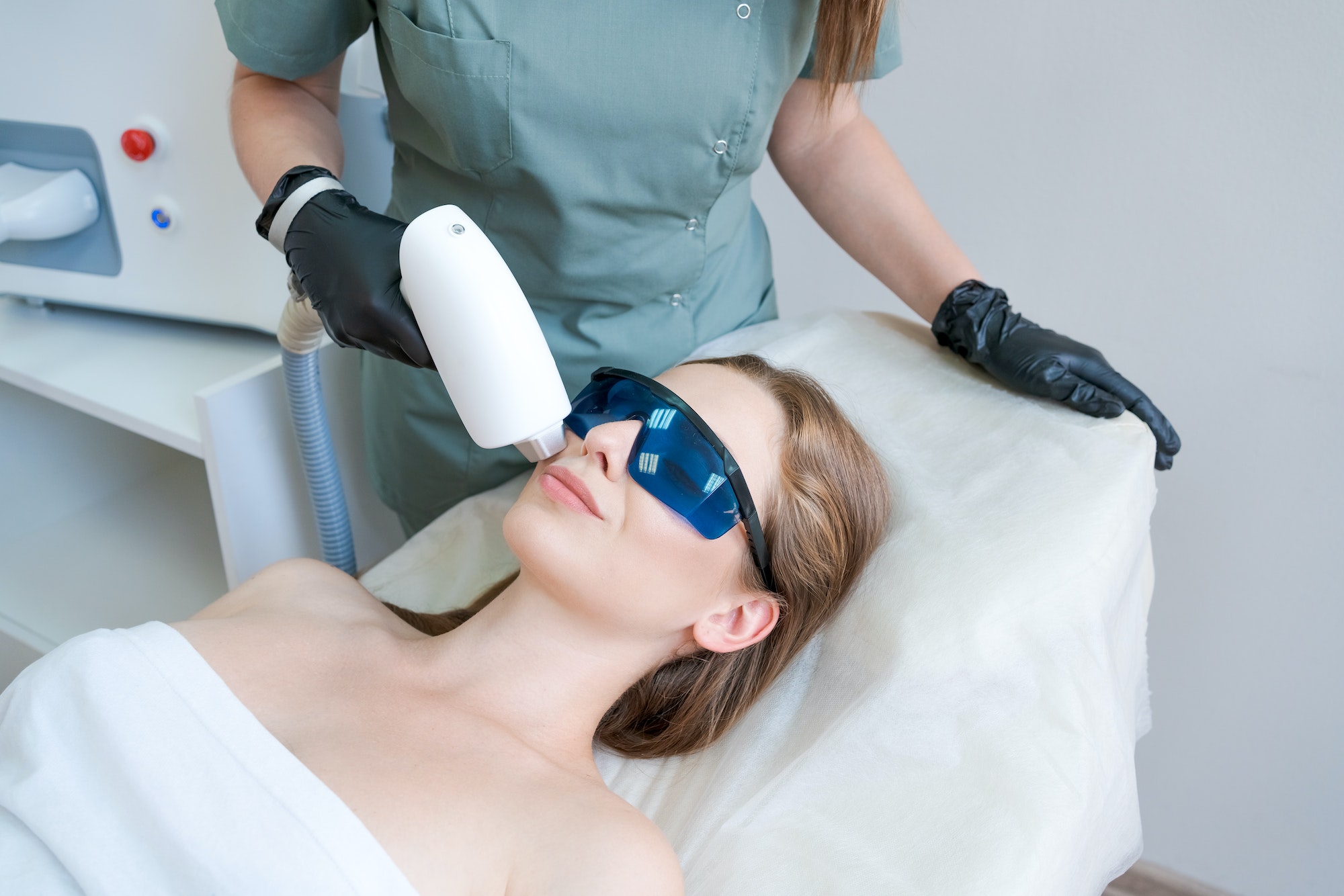 Therapist cosmetologist undergoes laser treatment on face young woman in beauty