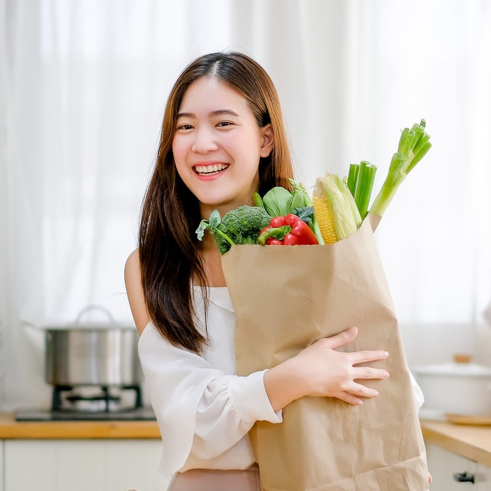 Lovely girl hold bag with various vegetables and smile stand in kitchen