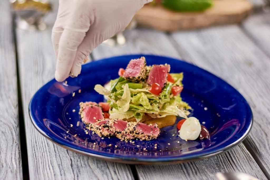 Chef hands sprinkling sesame on salad with tuna