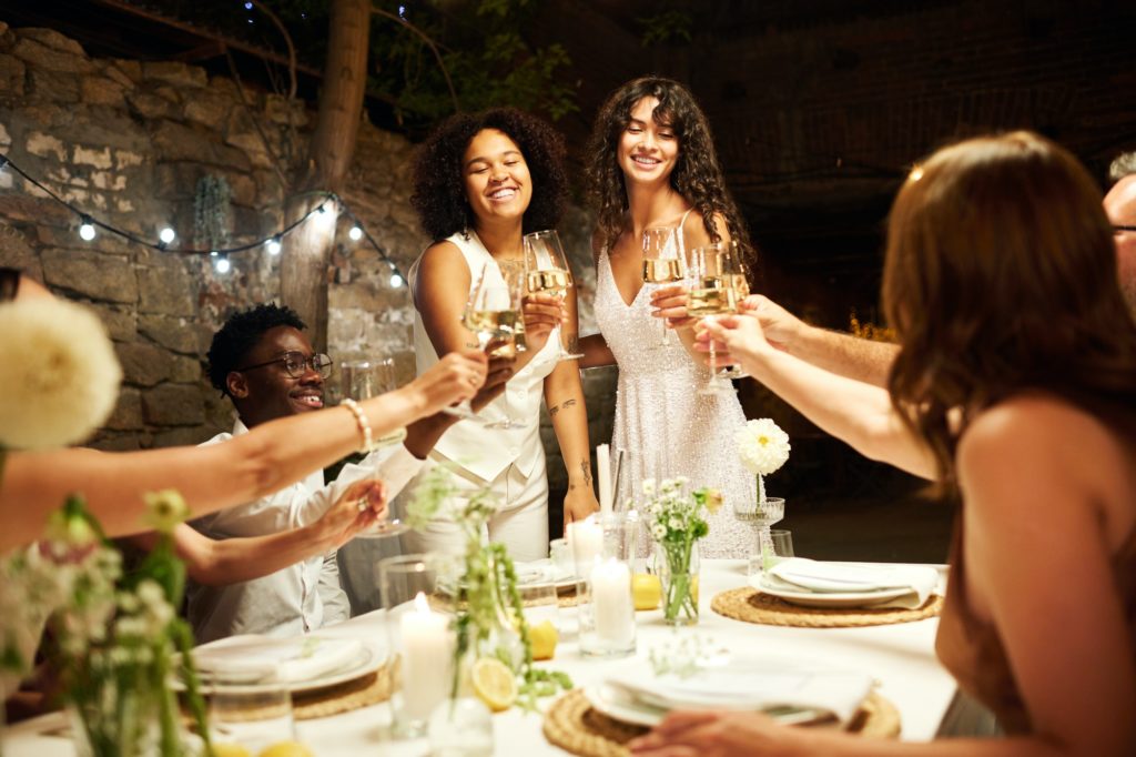 Two happy young intercultural brides toasting with their wedding guests