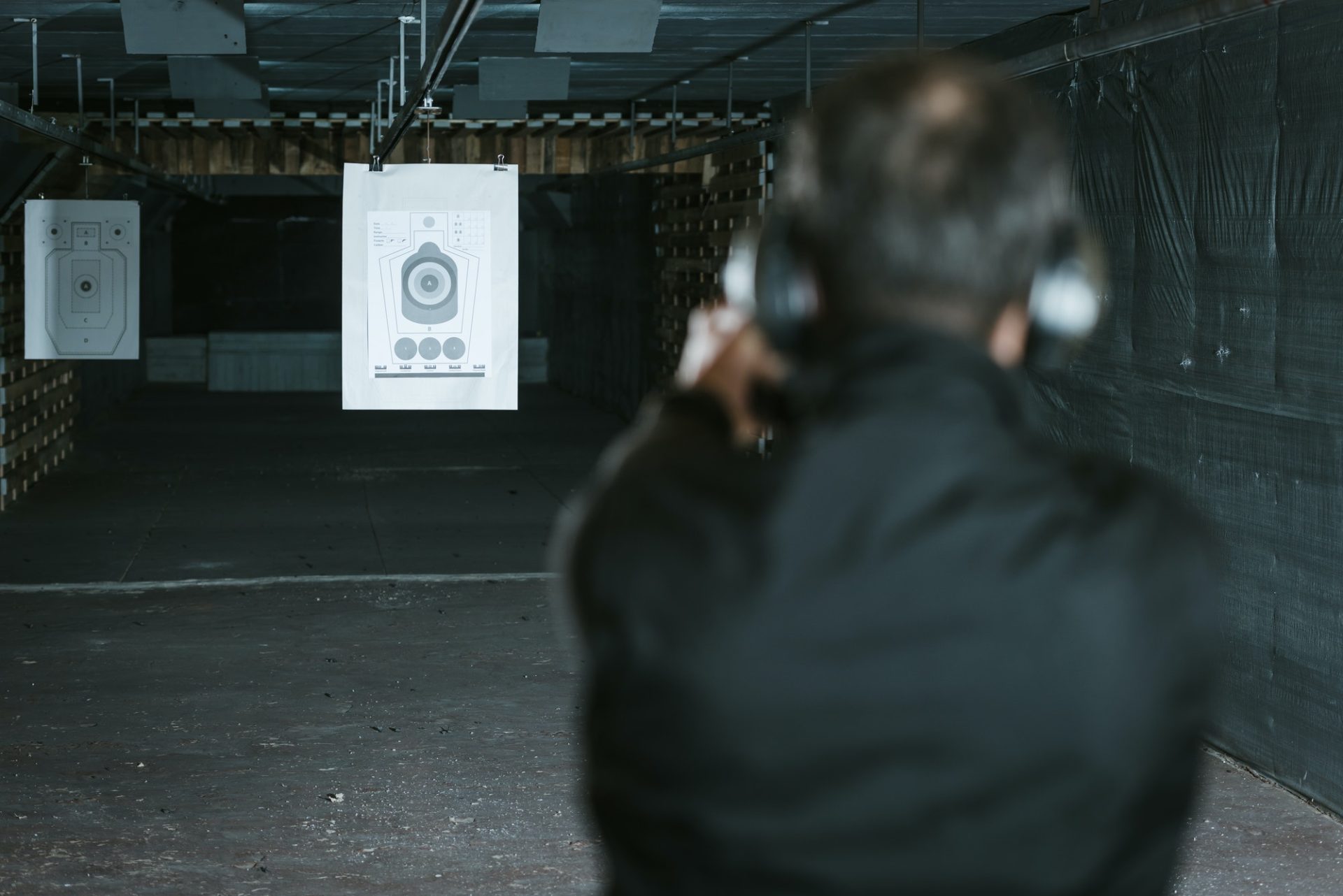 rear view of man aiming gun at target in shooting range