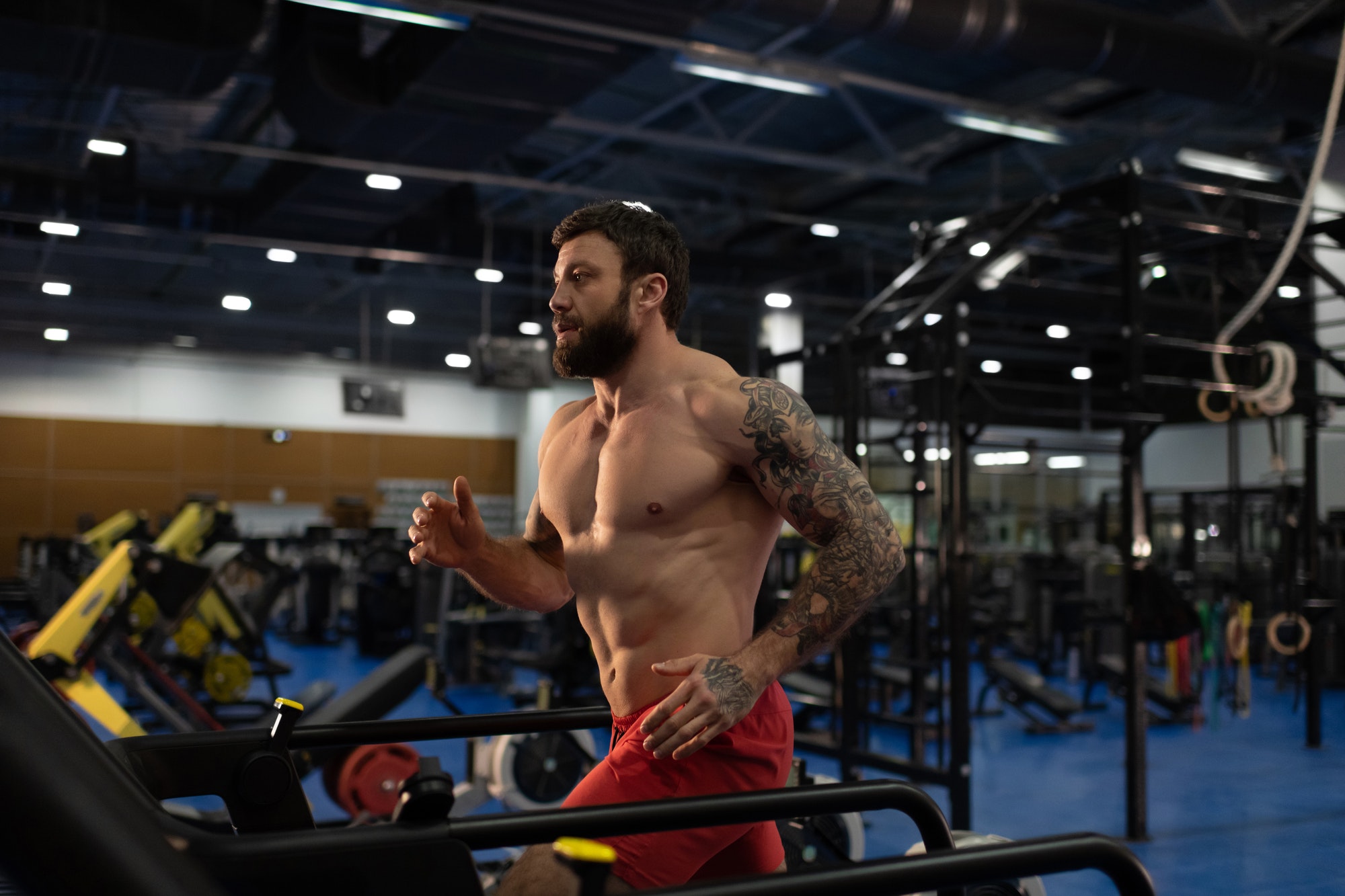 Strong male athlete running on modern treadmill