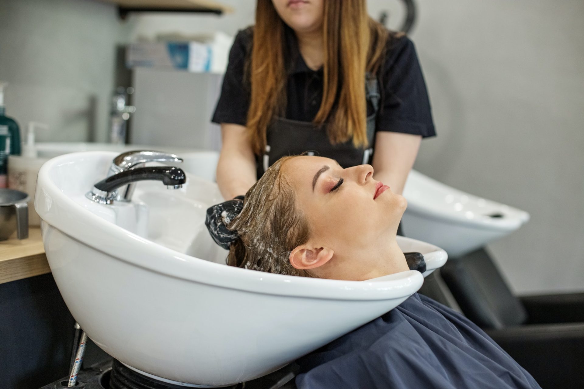 Hairdresser washes hair of client in hairdressing salon.