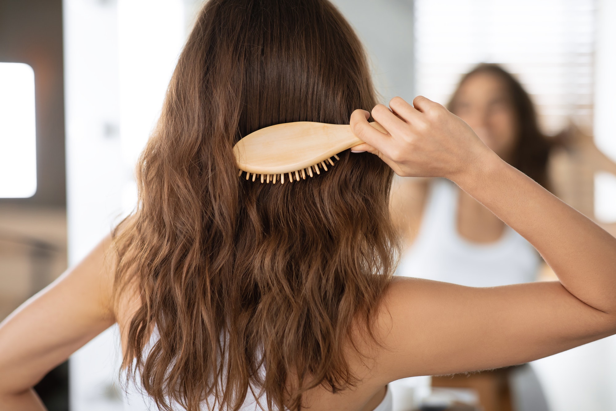 Lady Brushing Hair With Wooden Hairbrush In Bathroom, Rear View