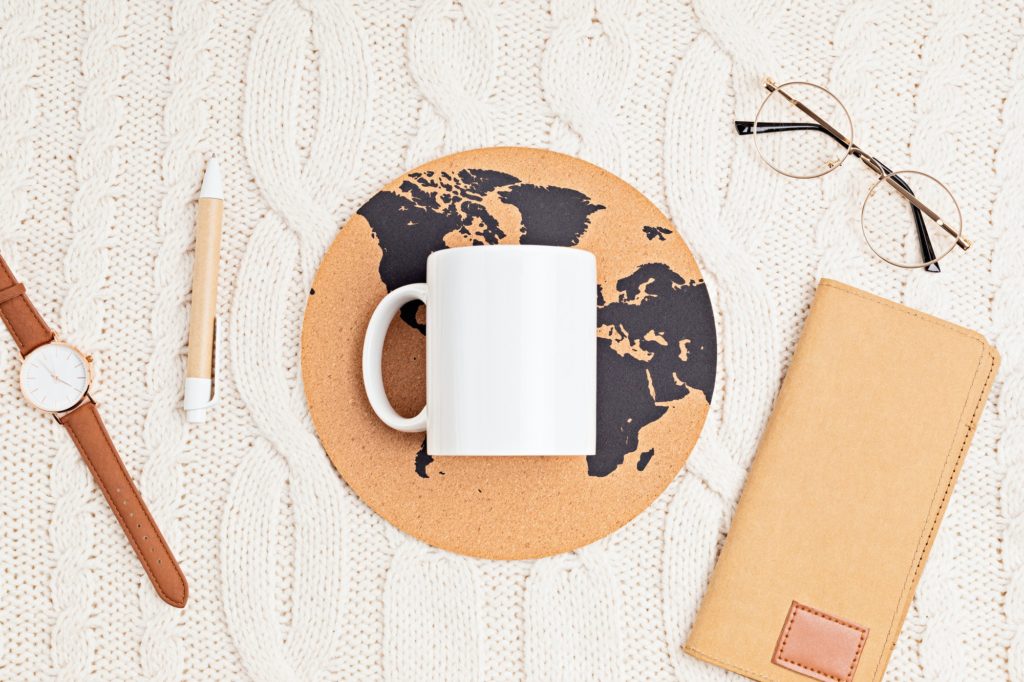 Mockup with white mug, glasses, watch, pen, notebook and globe print on white knitted background