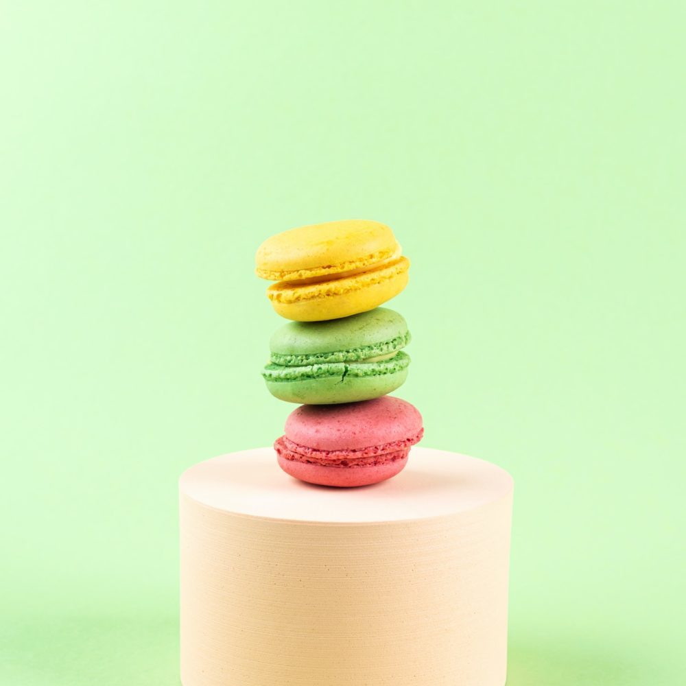 Geometric pastel green background with colorful macaroon sweet candies on circle podium