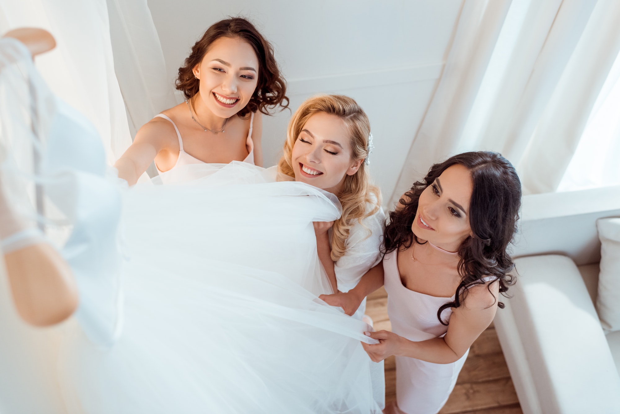 beautiful excited bride with bridesmaids touching wedding dress