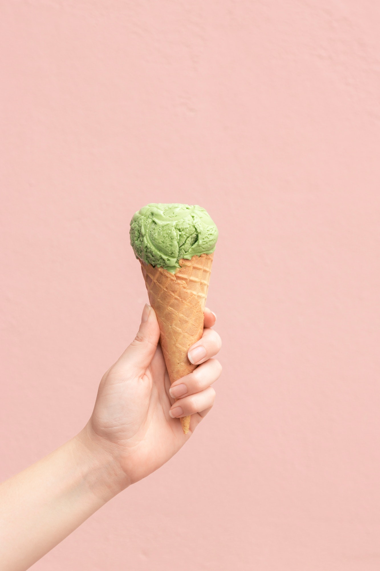 Woman holding a matcha ice cream cone against a pink wall