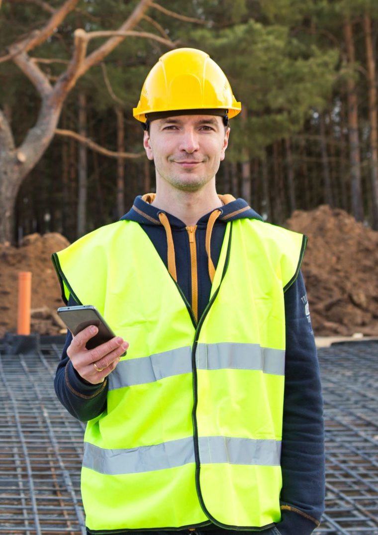 Construction worker talks on a smartphone in a yellow helmet and protective vest