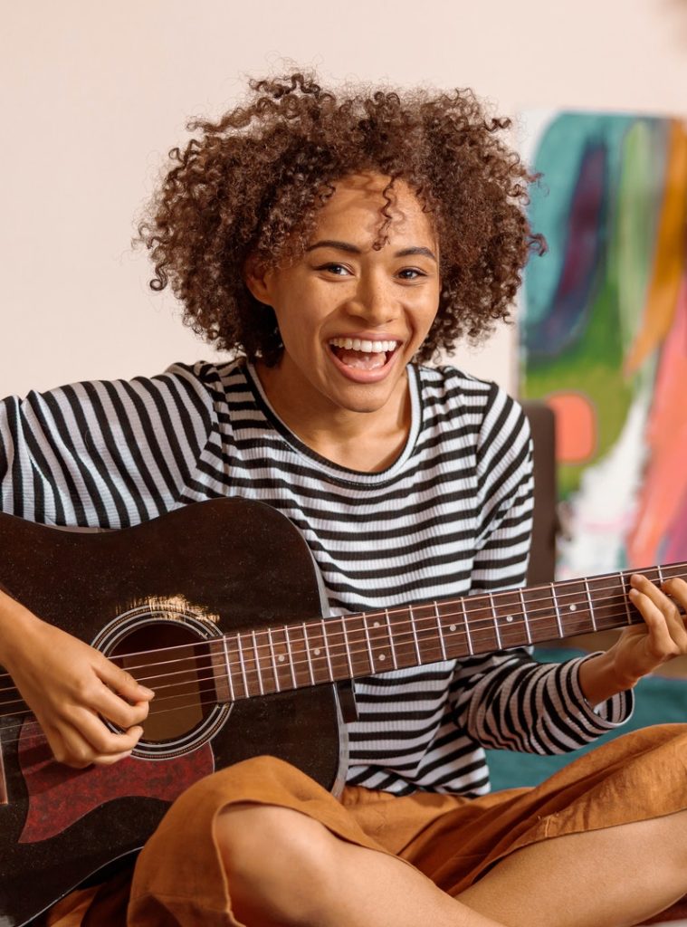 Cheerful African woman playing guitar at home