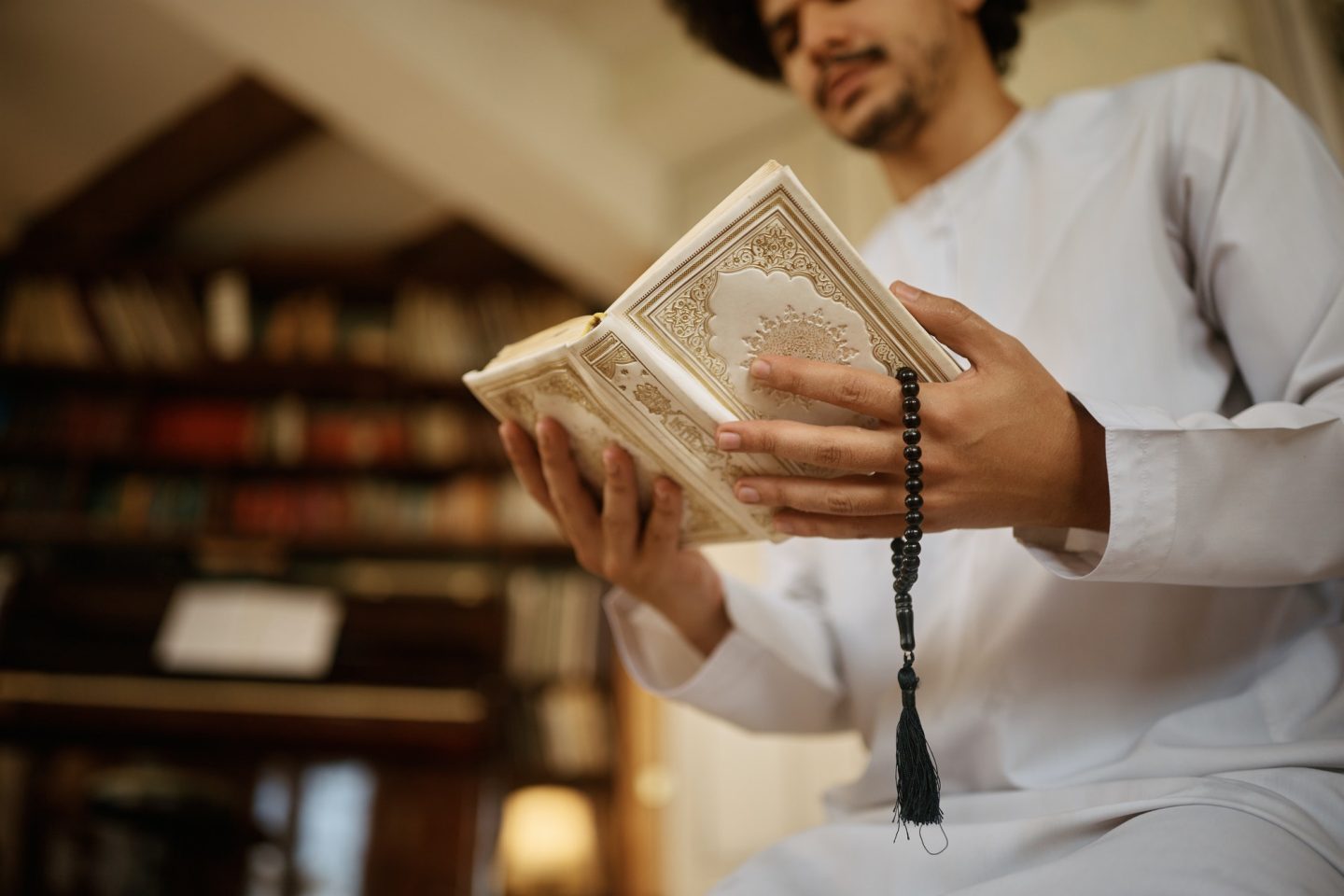 Close up of Muslim holding misbaha beads while reading Quran during prayer at home.