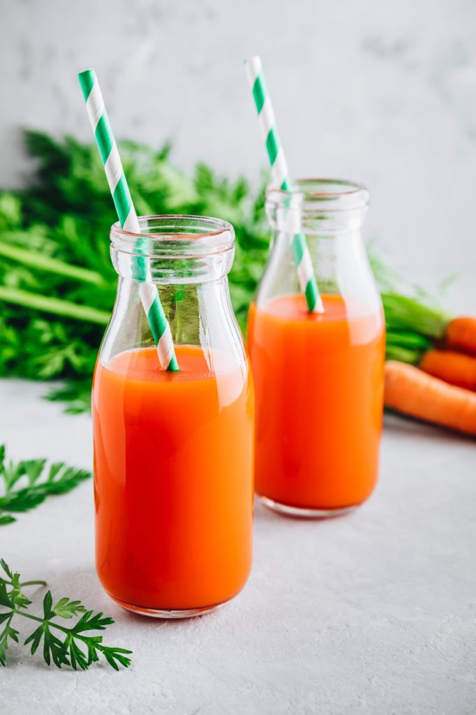 Fresh detox carrot juice in glass bottles on a gray stone background