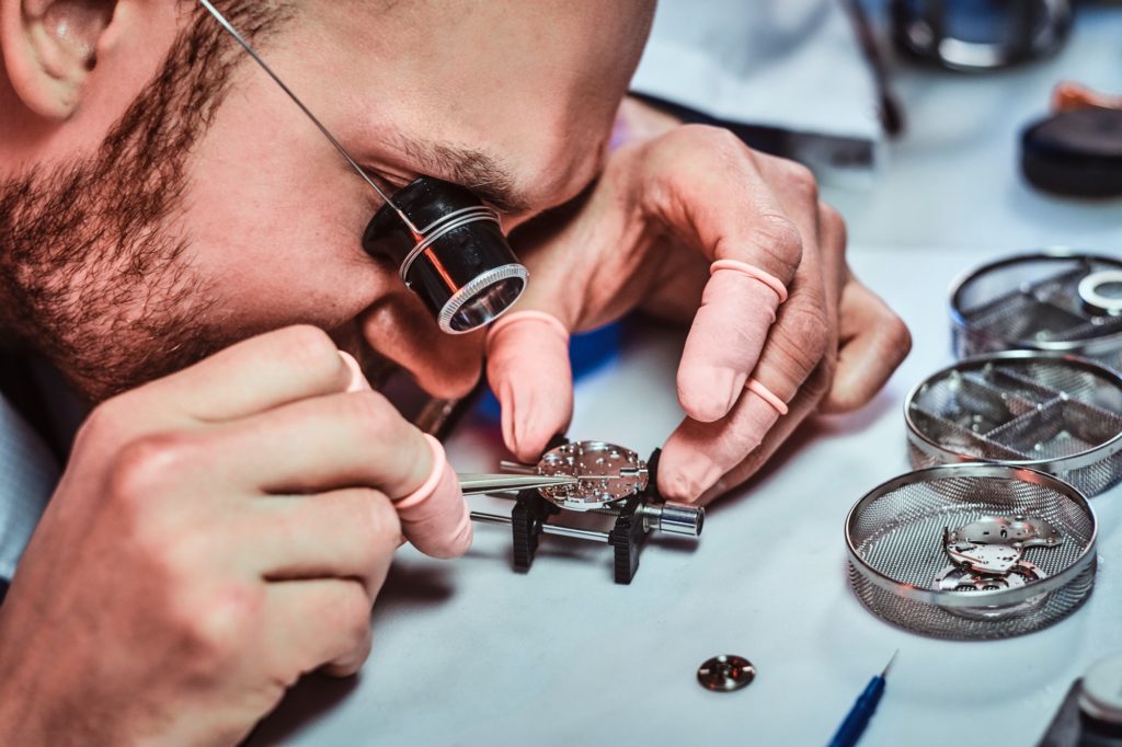 Expirienced clockmaster is fixing old watch for a customer at his repairing workshop