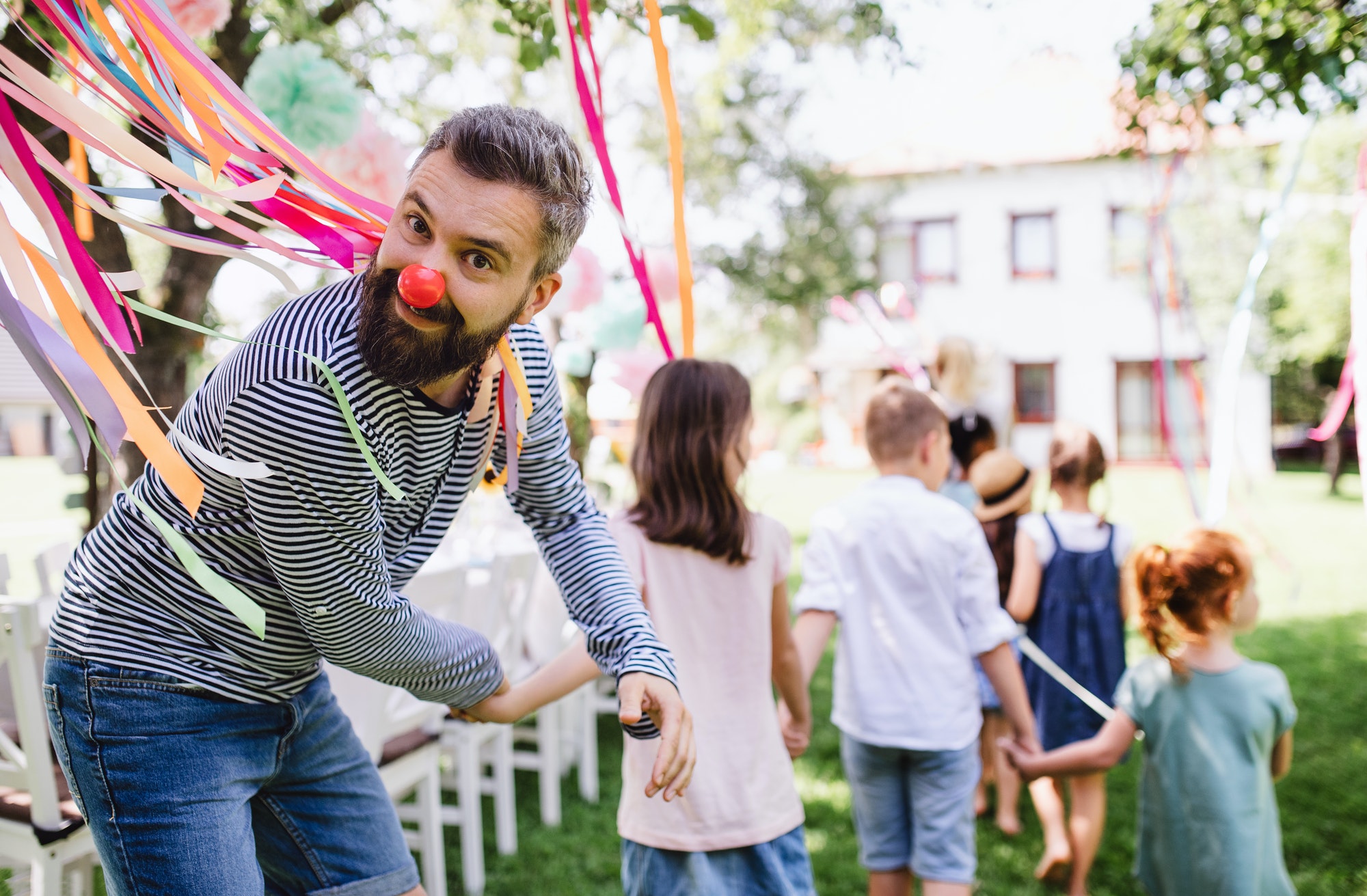 Man with kids on birthday party playing outdoors in garden in summer.