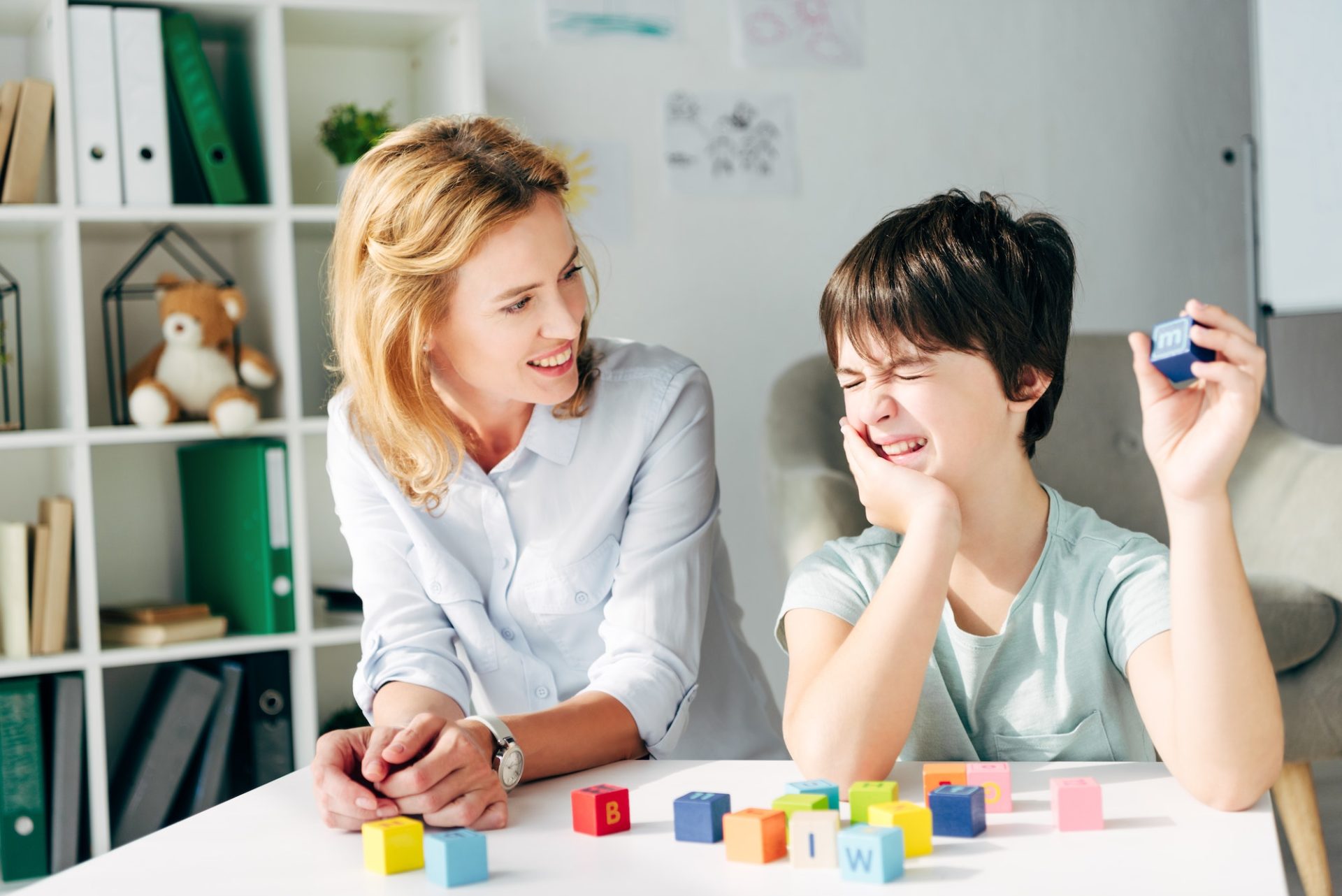 smiling child psychologist and kid with dyslexia playing with building blocks
