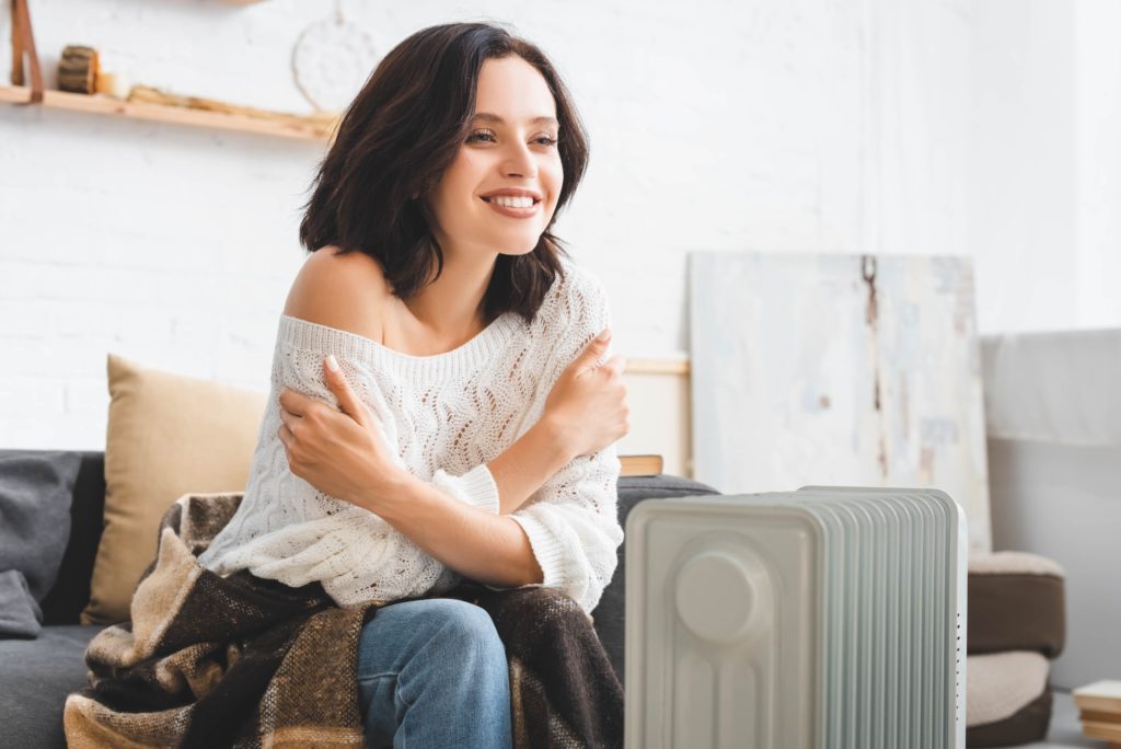 beautiful cheerful woman in cold room with heater