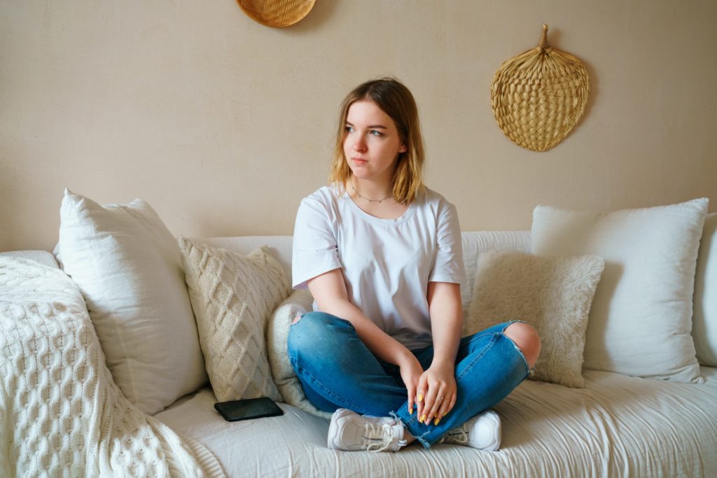 Stressed young woman sitting on sofa in casual clothes, worrying about problems