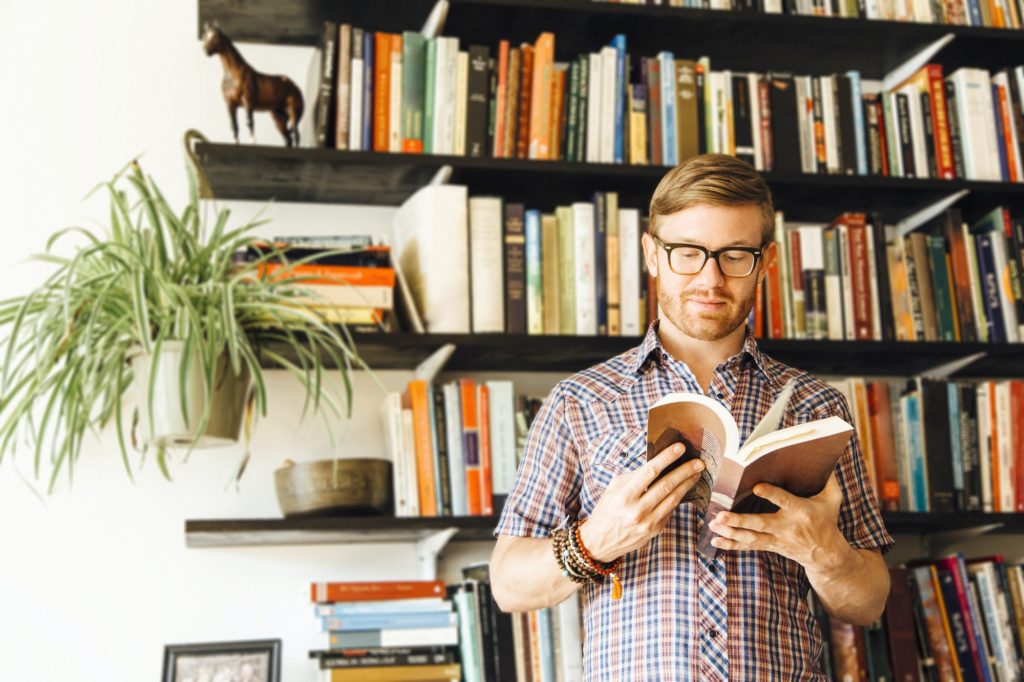 Mid adult man, standing in front of bookshelf, reading