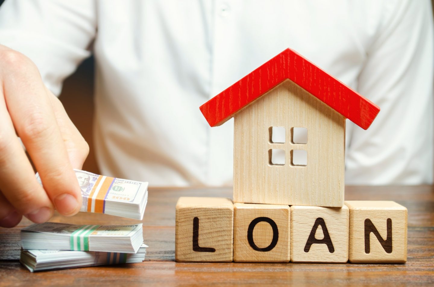 Wooden blocks with the word Loan, house and money in the hands of a businessman