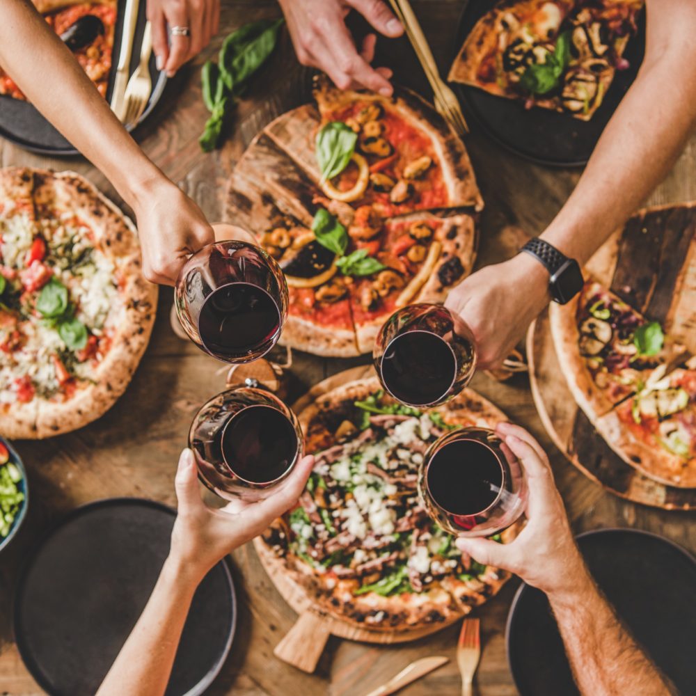 People clinking glasses over table with Italian pizza, square crop