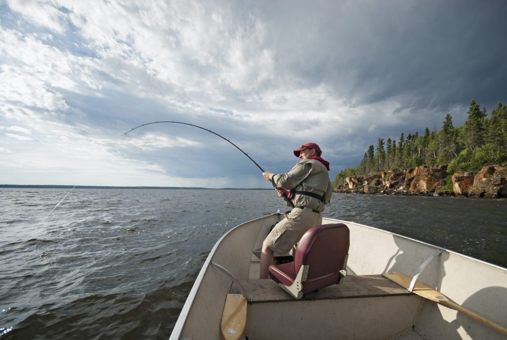 A man fishing from an open boat offshore with fish on the line.