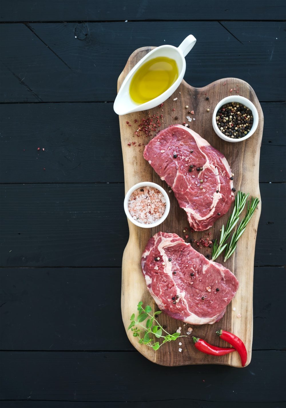 Raw fresh meat Ribeye steak entrecote and seasonings on cutting board over dark wooden background.