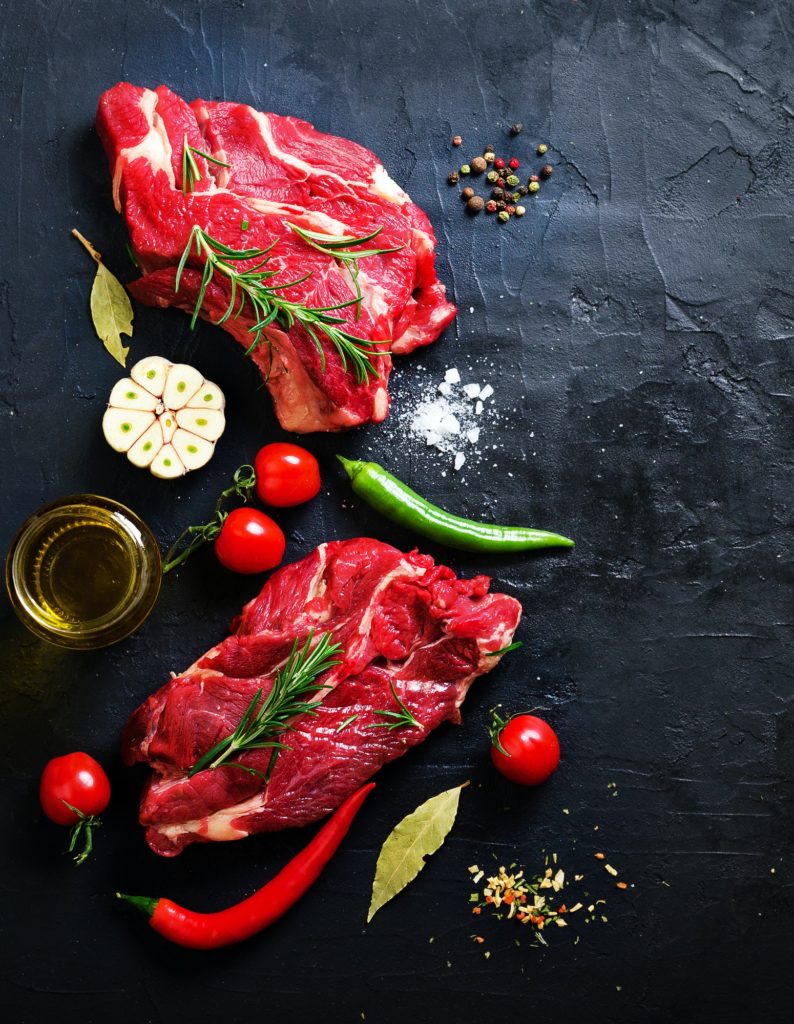 Raw meat, beef steak on a stone cutting board with rosemary, spices, salt, oil, cherry tomatoes, hot