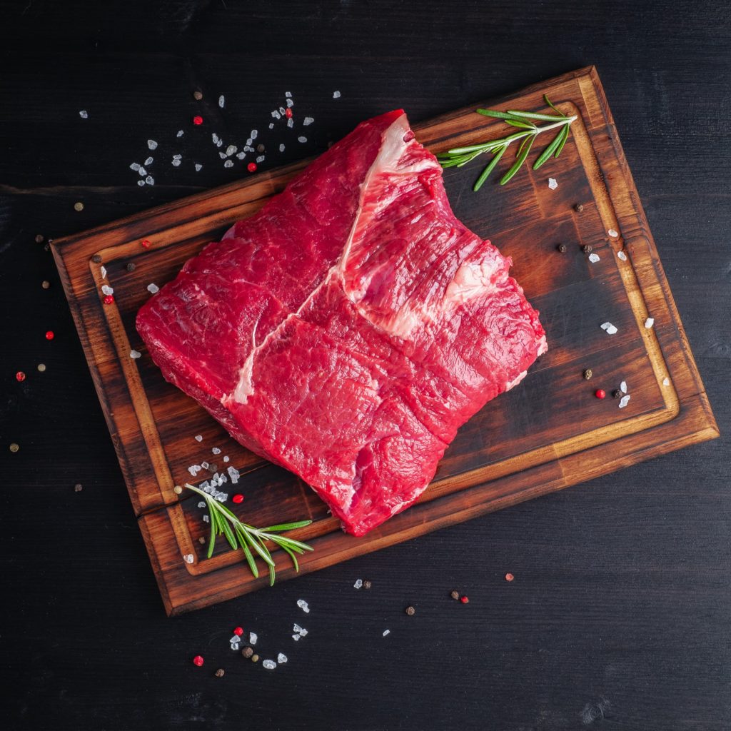 Raw meat, beef steak with seasoning on chopping board on dark background with rosemary,
