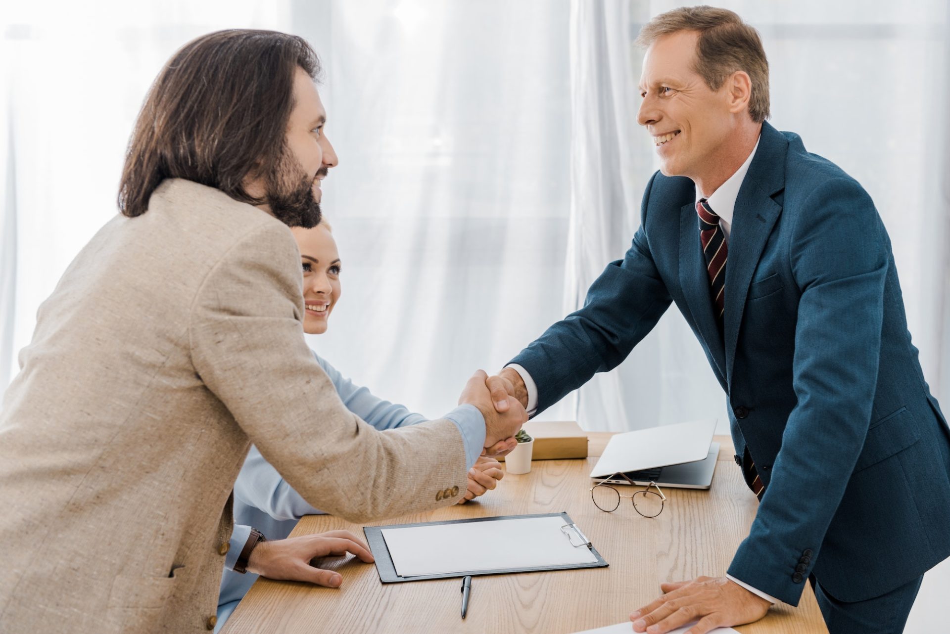 happy man and insurance agent shaking hands in office