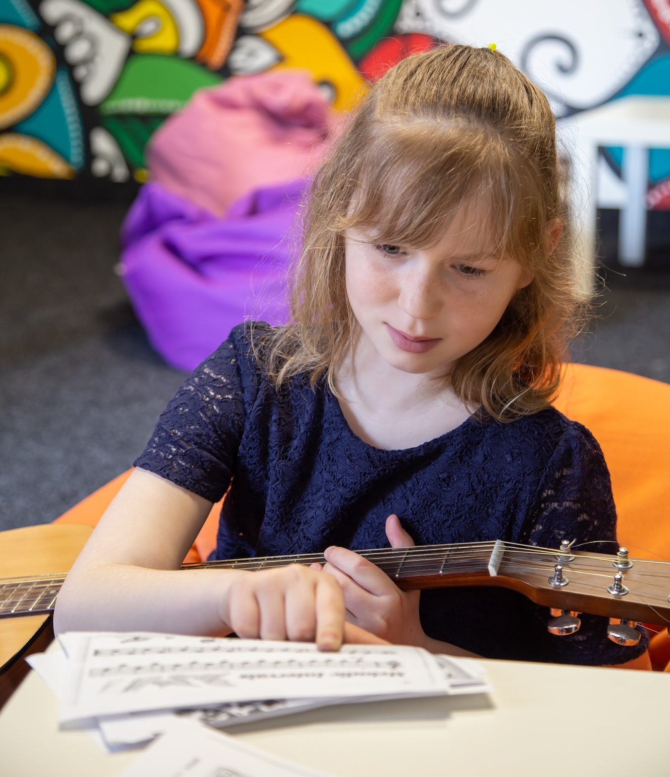 A little girl learns to play the guitar by sheet music.