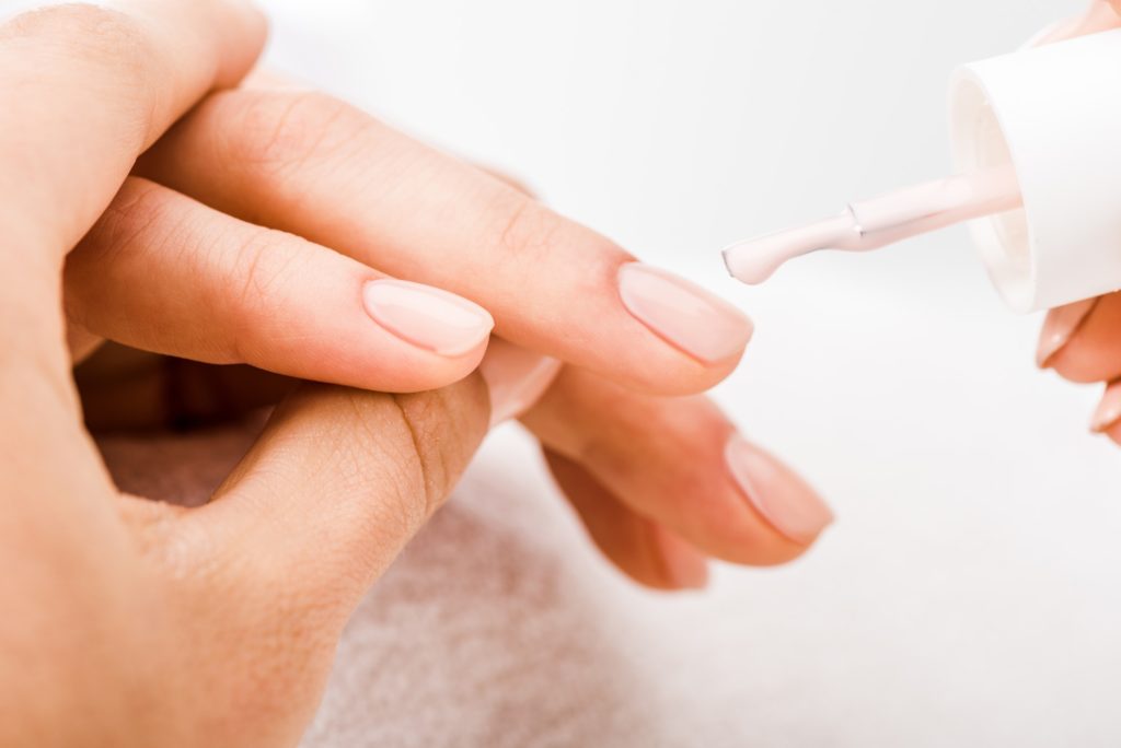 Cropped view of manicurist holding hand and applying nail polish on fingernails