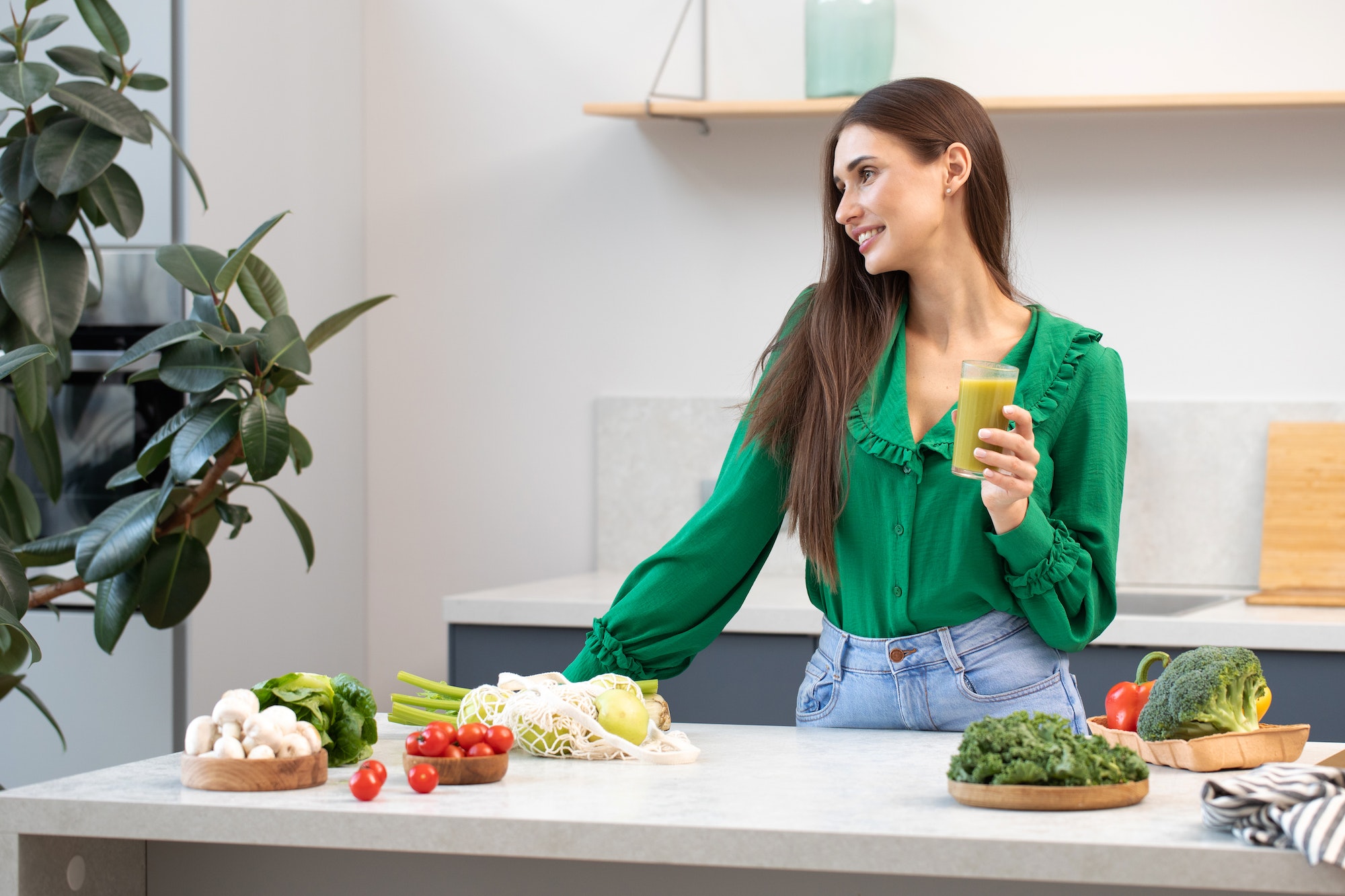 An attractive woman is standing in the kitchen with a glass of green smoothie. Healthy eating