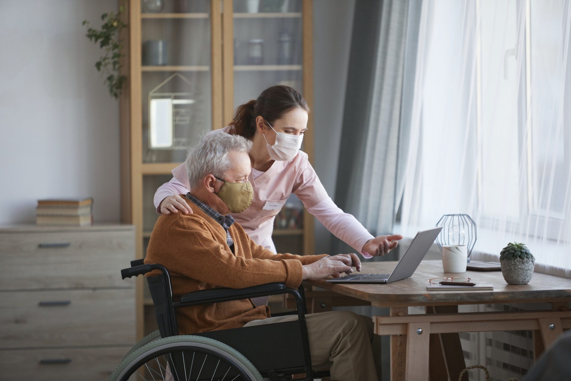 Disabled Senior Man Using Laptop with Caregiver Assisting