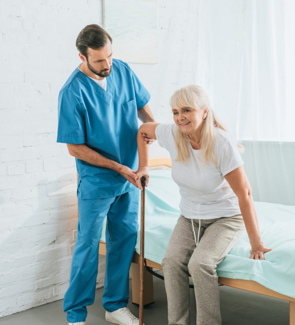 male nurse helping senior woman with walking stick