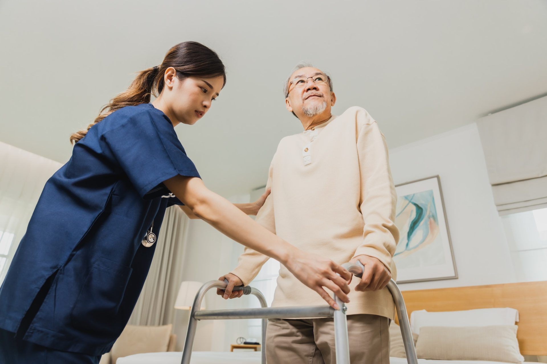 Smiling nurse woman helping senior Asian man to walk around the nursing home