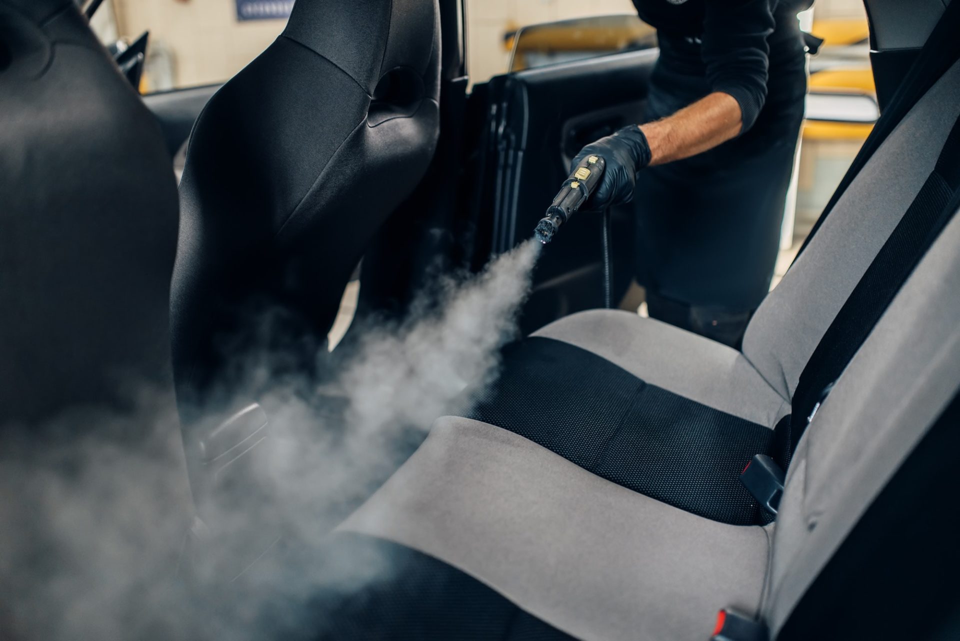 Carwash, worker cleans seats with steam cleaner