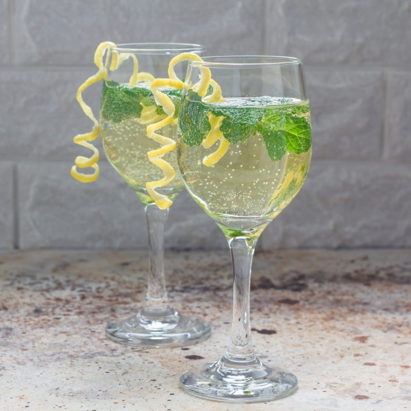 Spritzer cocktail with white wine, mint and ice, decorated with spiral lemon zest, square format