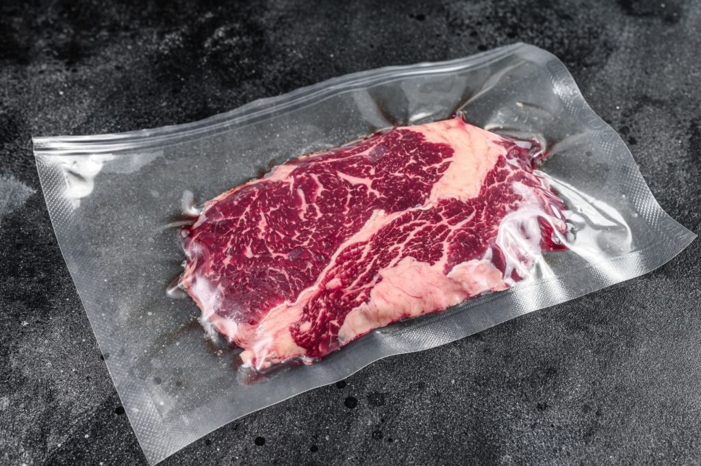 Raw rib eye beef meat steak in vacuum packaging. Black background. Top view