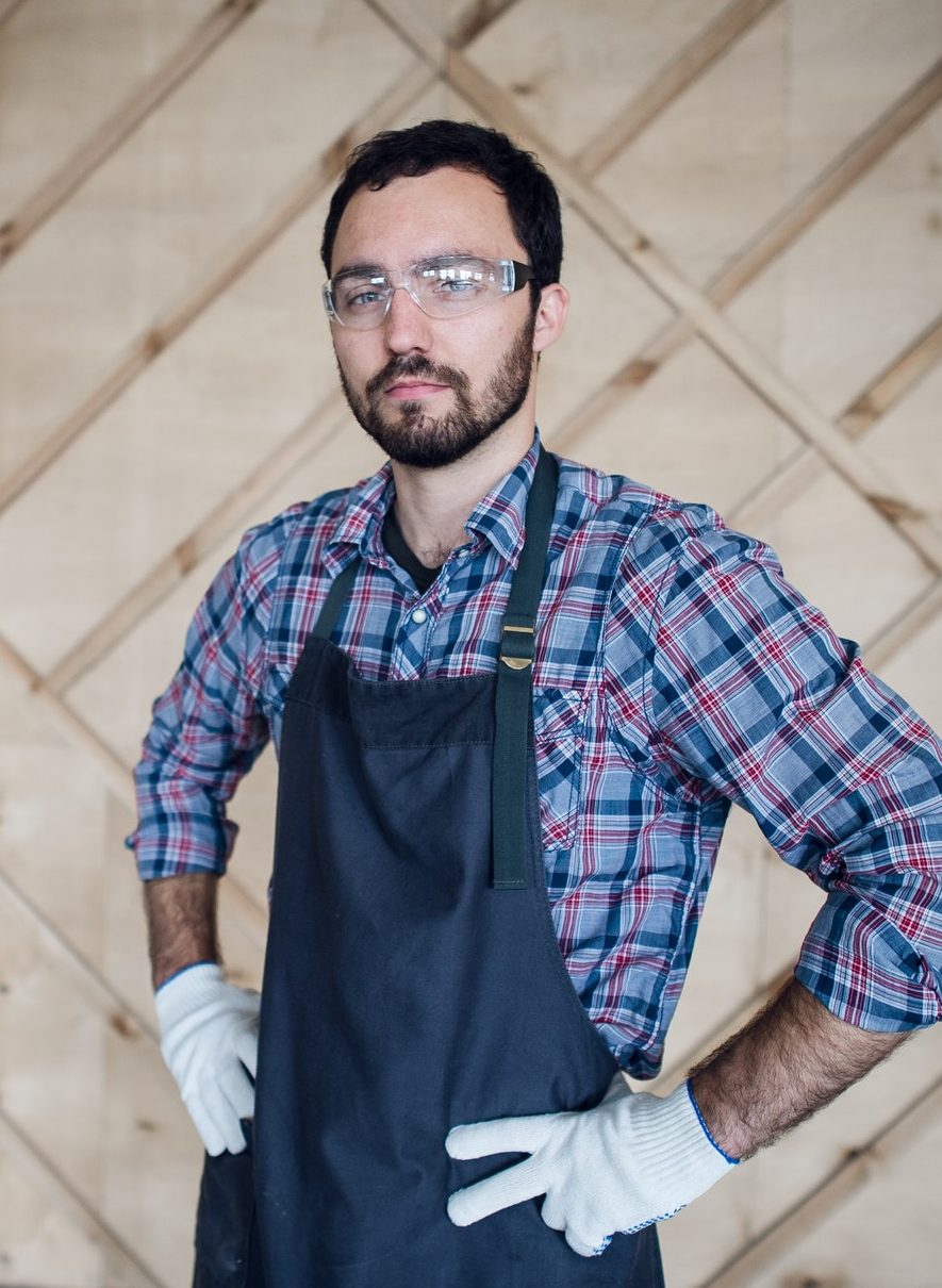 Young male carpenter wearing gloves and glasses with hands on hips