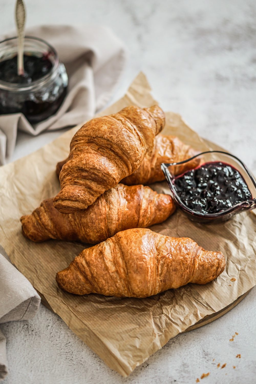 French fresh croissant with blackberry jam on a bakery paper and grey background