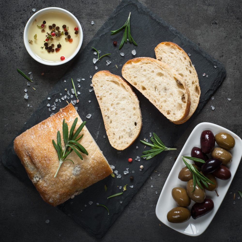 Italian ciabatta bread on black slate with herbs and olives.