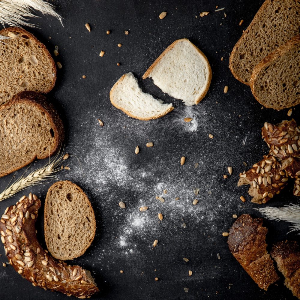 top view of breads as white, rye, bagel with sunflower seeds and wheat on black background
