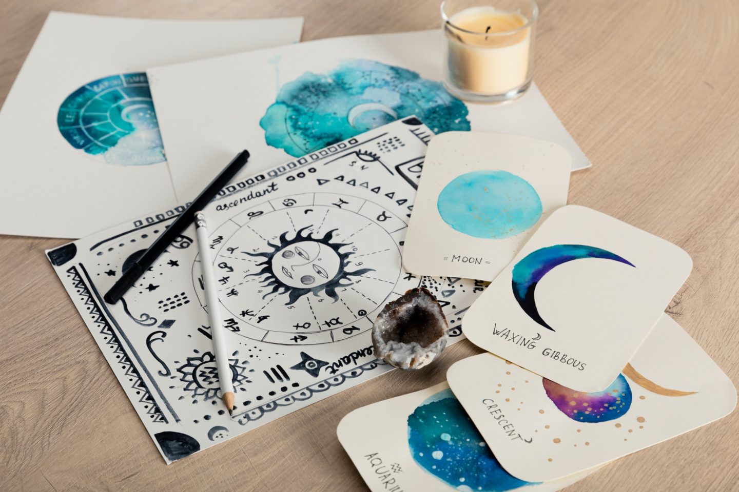 Selective focus of birth chart and cards with watercolor drawings of moon phases and candle on table