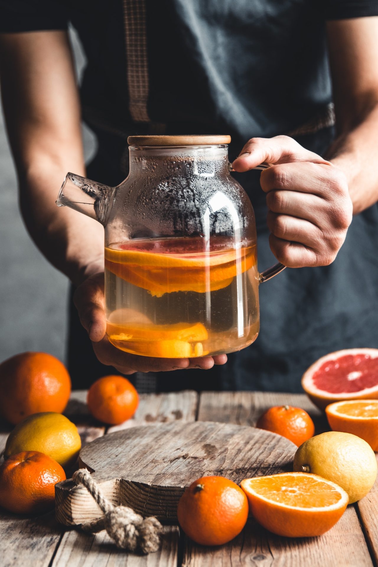 A man pours citrus tea on a wooden table. Healthy drink, vintage style. Vegan, eco products