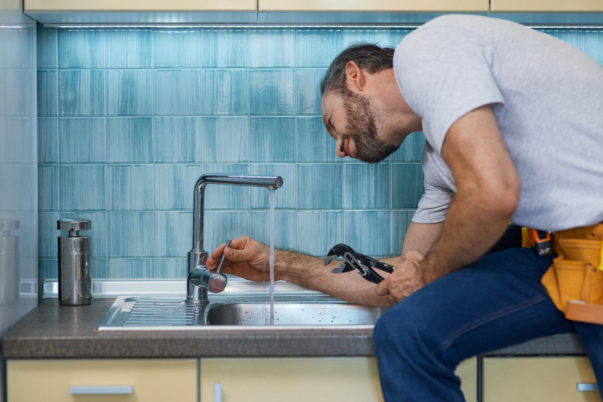Professional plumber looking concentrated, using pipe wrench while examining and fixing faucet in