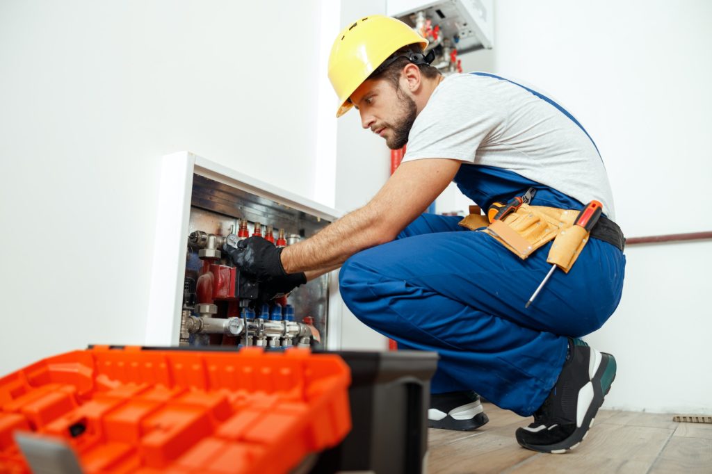 Side view of serious technician, plumber in uniform using tools from toolbox while checking water