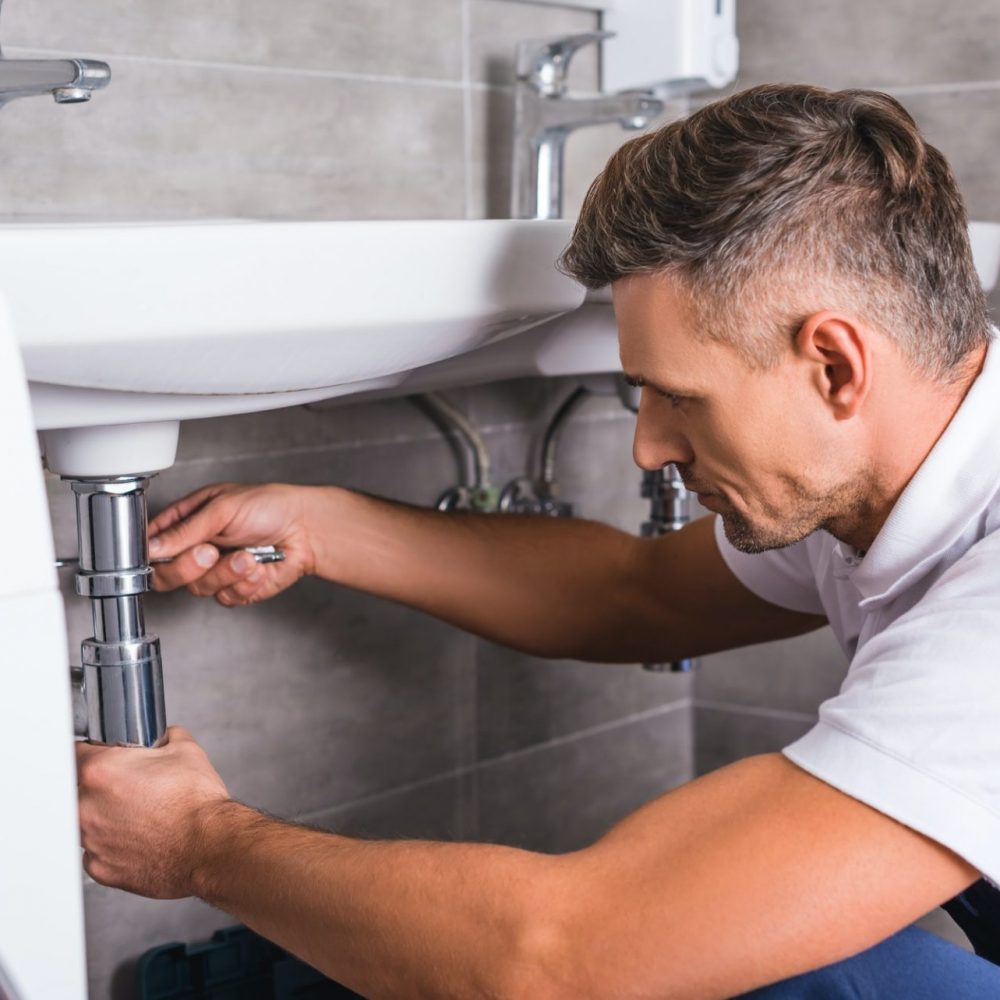 adult plumber fixing sink at bathroom