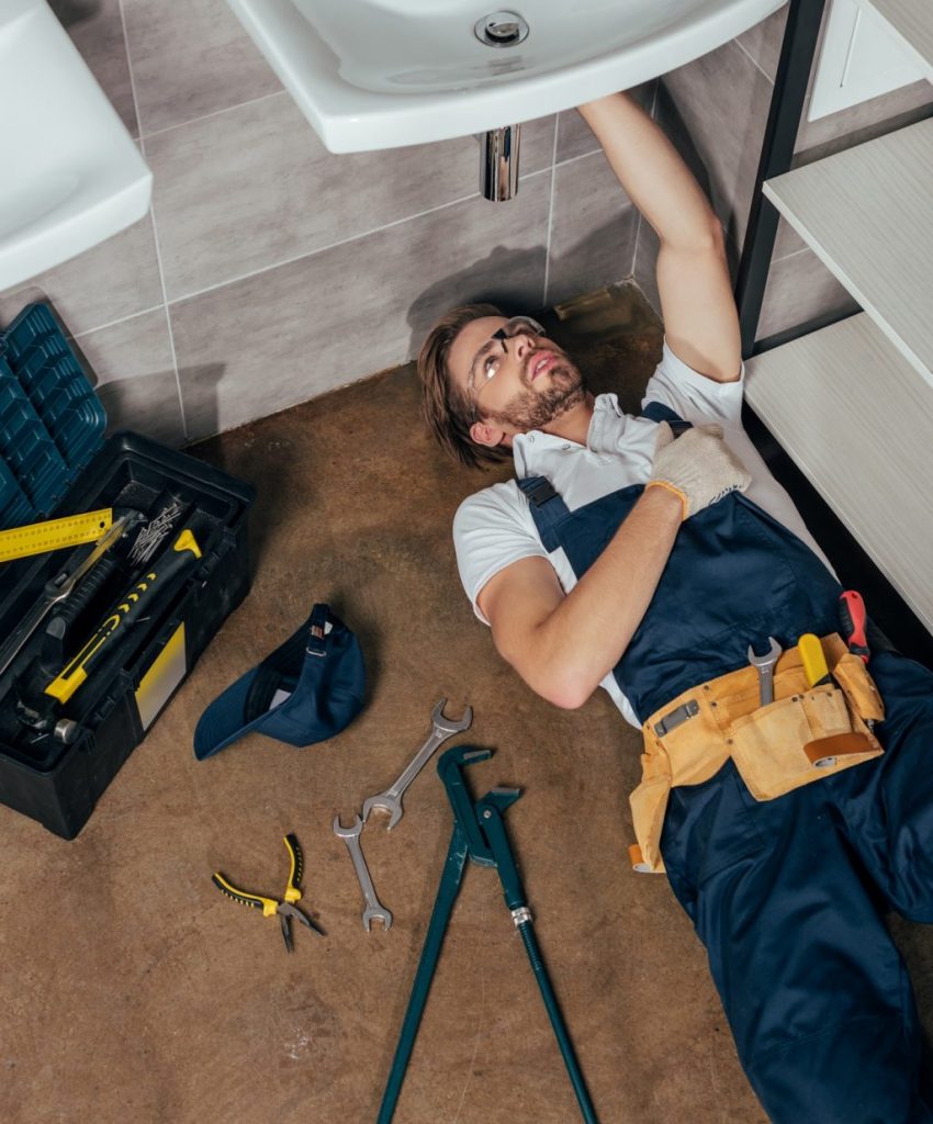 high angle view of young male plumber fixing sink in bathroom