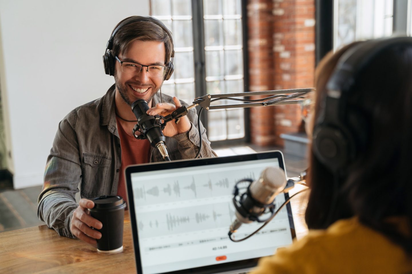 Smiling podcaster looking at camera while making audio podcast with his colleague