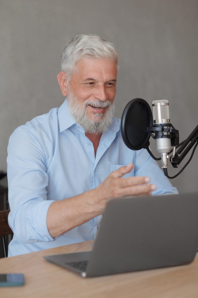 older man with gray hair irecording podcast in recording studio with microphone and headphones